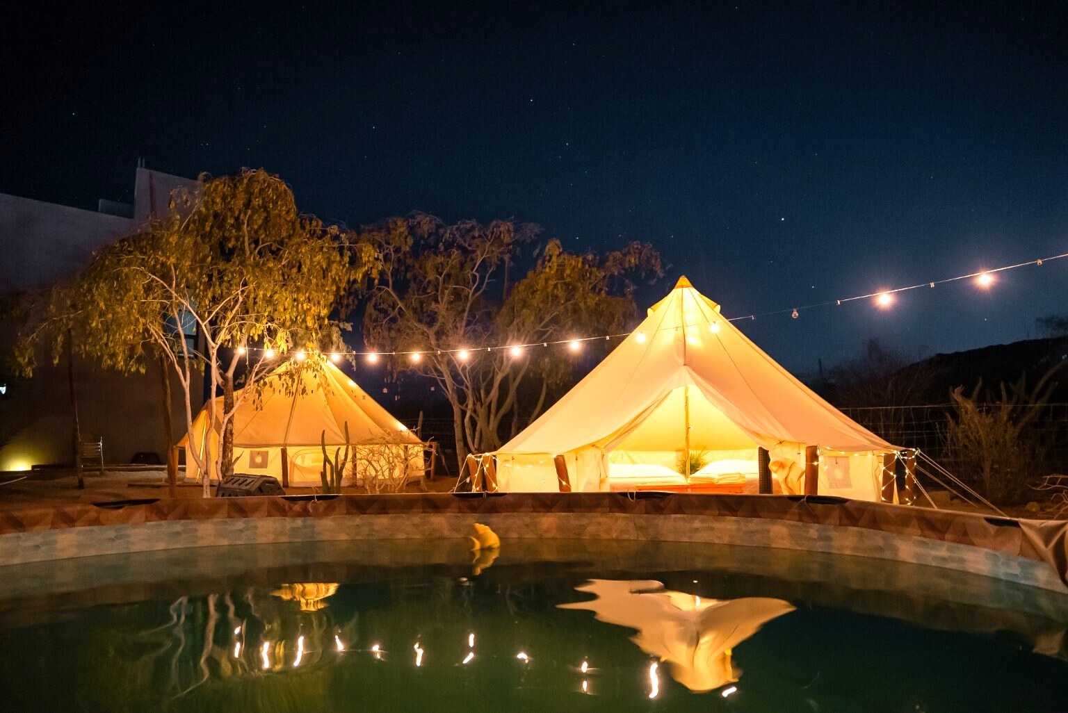 Glowing glamping tents reflected in the pool at night